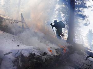 (Brittany Peterson | AP file photo) A member of the Mile High Youth Corps walks near a smoldering pile of tree debris during a controlled burn with the U.S. Forest Service in Hatch Gulch Wednesday, Feb. 23, 2022, near Deckers, Colo. U.S. Agriculture Secretary Tom Vilsack says the forest service conducted burns, tree thinning and other work to reduce wildfire risks across 5,000 square miles last year.
