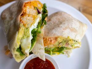 (Leah Hogsten | The Salt Lake Tribune) Even Stevens' Graduate Burrito, Dec. 22, 2021, with choice of bacon, ham, sausage or avocado, served with two eggs scrambled or medium cheddar, tots, house sauce, sriracha, tomatoes, onions and spinach with a side of salsa morita, $9.75.