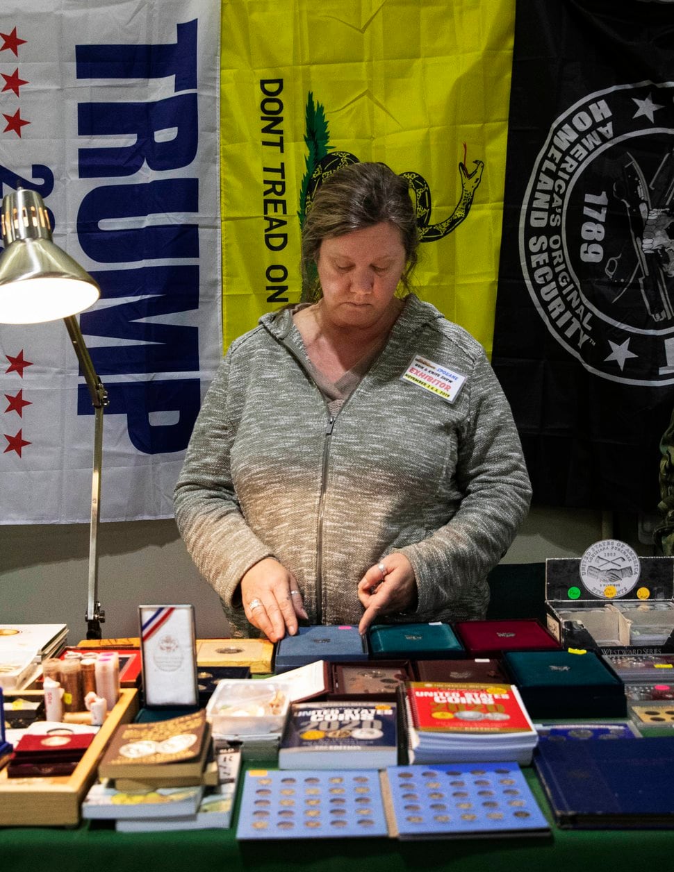(Ruth Fremson | The New York Times) Shanna Torp, who became concerned about her father’s state of mind after her mother died following heart surgery, works her family’s collectible coins booth at a gun and knife show in Spokane, Wash., Nov. 4, 2019. A year after the coronavirus pandemic began, the toll of self-inflicted gun deaths has led to an unusual alliance between suicide-prevention advocates and gun-rights proponents; together they are devising new strategies to prevent suicide in a population committed to the Second Amendment and the right to bear arms.