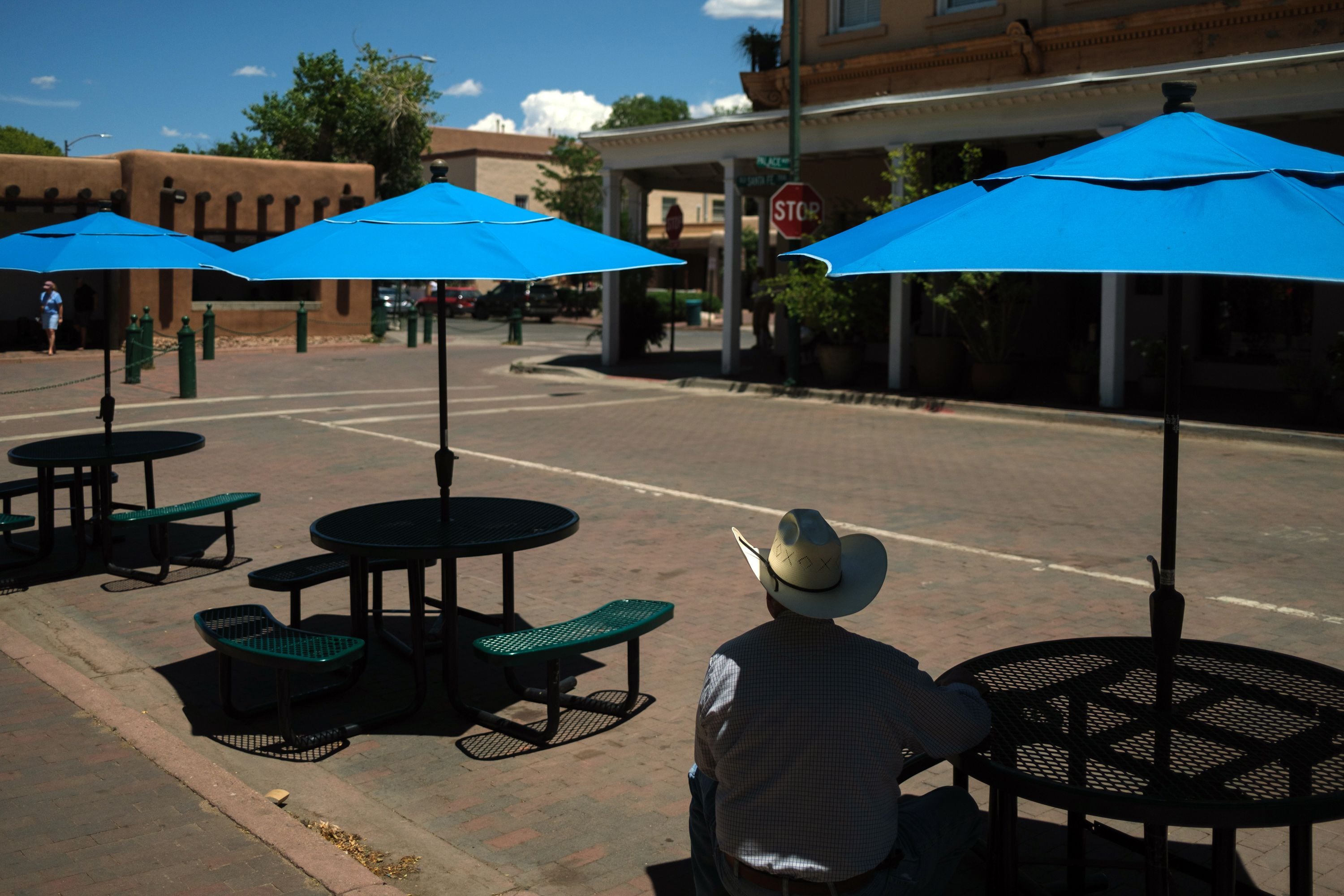 (Ramsay de Give | The New York Times) A man sits in the shade of an umbrella in Santa Fe Plaza in Santa Fe, N.M., on Monday, July 17, 2023.