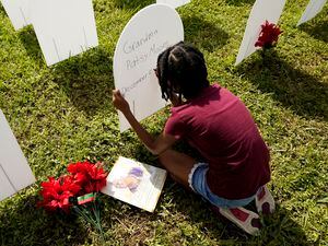 (Lynne Sladky | AP) In this Nov. 24, 2020, photo, Kyla Harris, 10, writes a tribute to her grandmother Patsy Gilreath Moore, who died at age 79 of COVID-19, at a symbolic cemetery created to remember and honor lives lost to COVID-19 in the Liberty City neighborhood of Miami. A new novel, “The Maiden of All Our Desire,"  examines the plague during the 1300s for clues to the world's cultural moment.