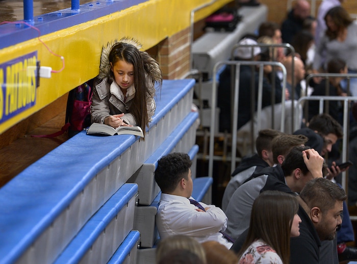 (Leah Hogsten | The Salt Lake Tribune) Addison Meza, 10, reads a Harry Potter book atop the bleachers as her brother, Cyprus High School basketball player Cody Mesa competes during a regular season game. Cyprus High School has grown and changed since the gym and what may be the state's oldest operating indoor pool were constructed in 1955. A new school is in the works, badly needed to accommodate a growing population on the west side's close-knit community, where long-time fans show up no matter how good or bad the Pirates are.