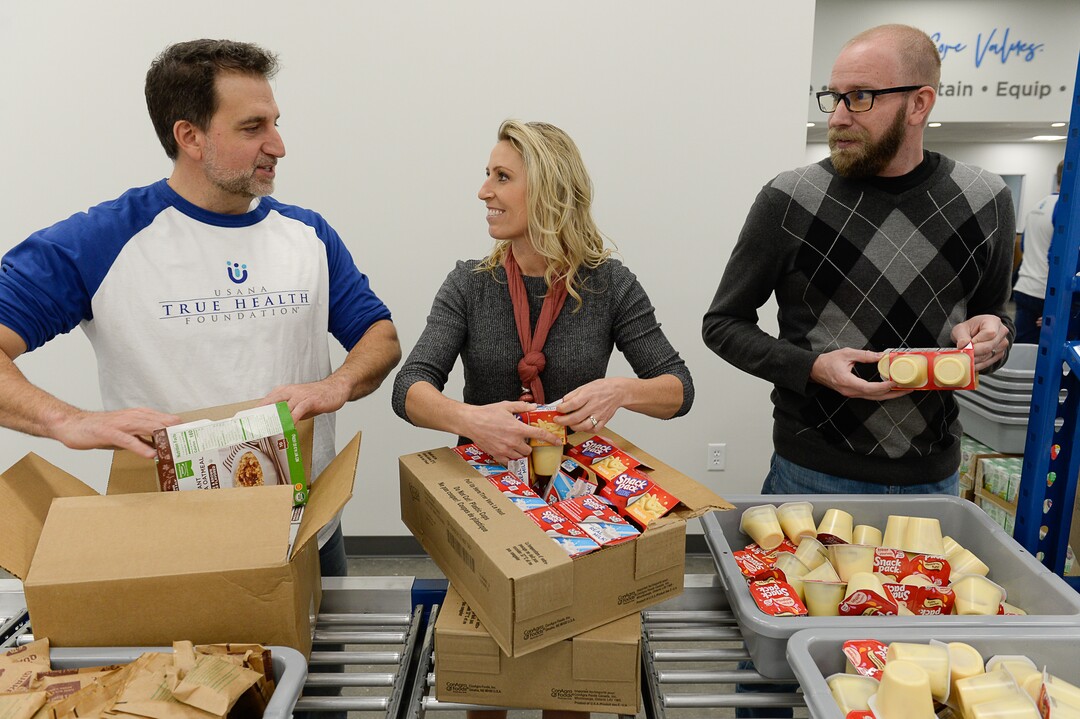 (Francisco Kjolseth  |  The Salt Lake Tribune)  Michelle Benedict, who founded Kids Next Door and is now the engagement manager for USANA Kids Eat, pitches in restocking the line alongside her husband Peter, left, and Aaron Swensen as USANA staff volunteer their time assembling food bags for at-risk youth at the newly-renovated packing and storage facility next to the headquarters of the Salt Lake City company on Wed. Dec. 11, 2019. The USANA Foundation has acquired two local charities, Kids Next Door and KidsEat!, that provides hundreds of food bags every week for the kids for the weekends and during long school breaks.