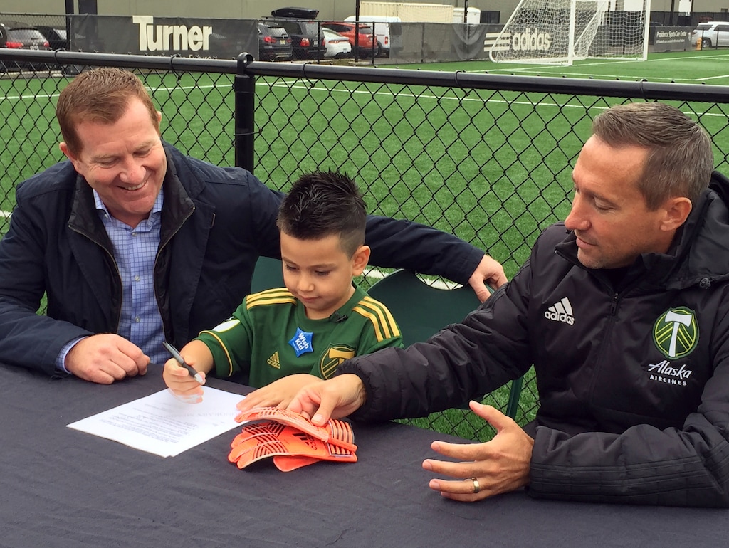 Five-year-old Derrick Tellez, center, signs his contract with Portland Timbers general manager Gavin Wilkinson, left, and coach Caleb Porter, right, on Friday, Sept. 22, 2017, at the Timbers’ practice facility in Beaverton, Ore. Tellez, who has had three surgeries for a cancerous brain tumor, was signed to a one-game contract with the MLS soccer team, granting his wish with Make-A-Wish Foundation Oregon. (AP Photo/Anne M. Peterson)