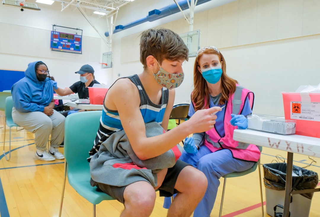 (Leah Hogsten | The Salt Lake Tribune) Parker Manning, 16, a student at Woods Cross High School, looks at his  Pfizer vaccination card after receiving his first shot from Pharmacist Shannon Stoker at a pop-up clinic by Nomi Health,  April 27, 2021. County and regional health districts are setting up vaccination clinics in high schools, to get the COVID-19 vaccine to 16 and 17-year-olds.