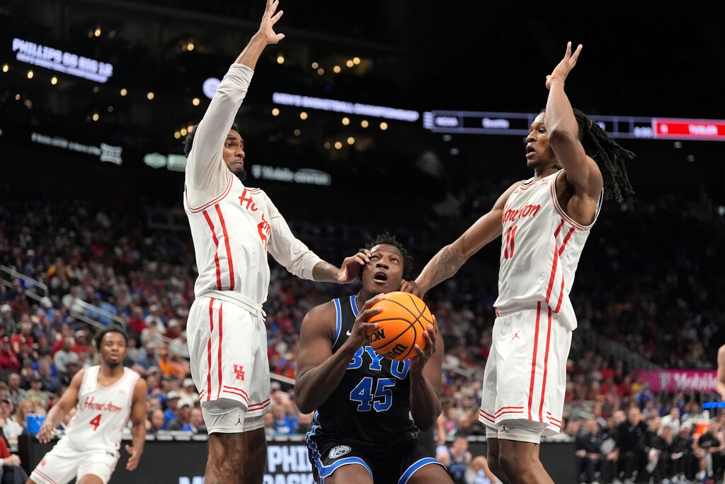 Brigham Young's Fousseyni Traore, center, looks to the basket between Houston's Mylik Wilson, left, and Joseph Tugler, right, during the first half of an NCAA college basketball game in the semifinal round of the Big 12 Conference tournament, Friday, March 14, 2025, in Kansas City, Mo. (AP Photo/Charlie Riedel)