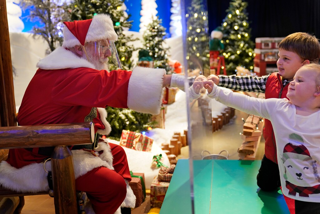 (AP Photo/Seth Wenig) Julianna, 3, and Dylan Lasczak, 5, visit with Santa through a transparent barrier at a Bass Pro Shop in Bridgeport, Conn., on Nov. 10, 2020. In this socially distant holiday season, Santa Claus is still coming to towns (and shopping malls) across America but with a few 2020 rules in effect.