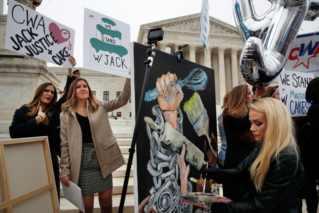 (AP Photo/Jacquelyn Martin) As Janae Stracke, left, and Annabelle Rutledge, both with Concerned Women for America, hold up signs, as Jessica Haas, of Indianapolis, paints during a rally with supporters of cake artist Jack Phillips outside of the Supreme Court which is hearing the 'Masterpiece Cakeshop v. Colorado Civil Rights Commission' today, Tuesday, Dec. 5, 2017, in Washington.