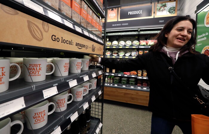 A customer reaches for a "Just Walk Out Shopping" mug at an Amazon Go store, Monday, Jan. 22, 2018, in Seattle. The store, which opened to the public on Monday, allows shoppers to scan their smartphone with the Amazon Go app at a turnstile, pick out the items they want and leave. The online retail giant can tell what people have purchased and automatically charges their Amazon account. (AP Photo/Elaine Thompson)