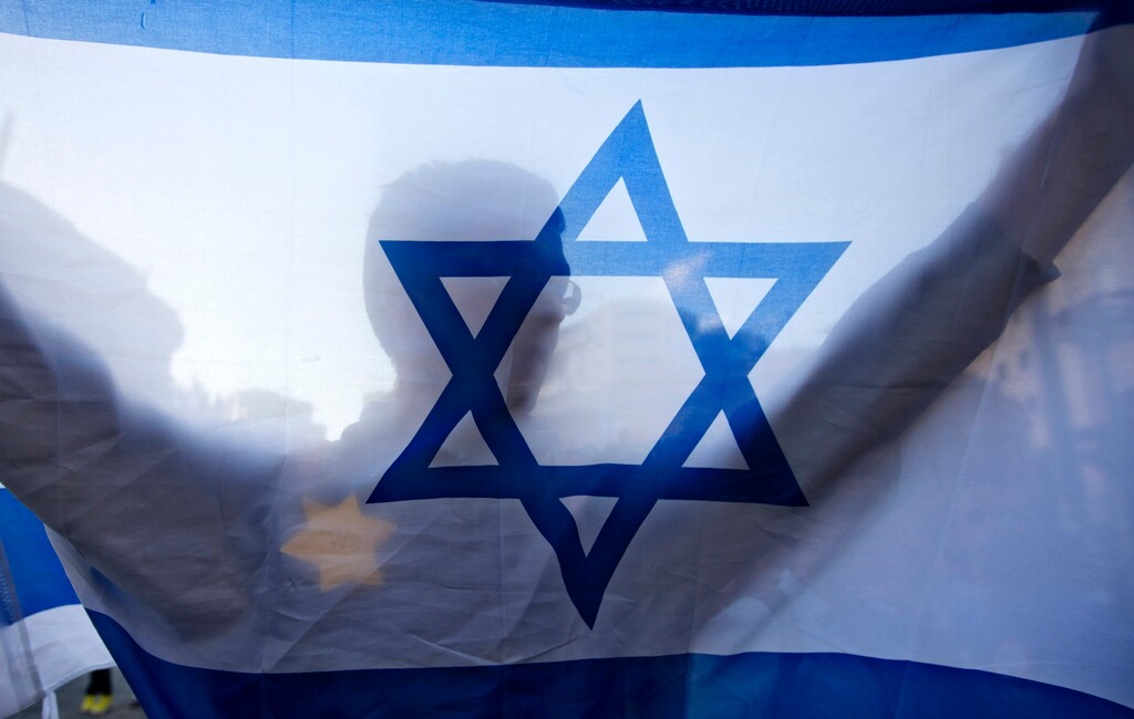 (Sebastian Scheiner | The Associated Press) In this July 14, 2014 photo, a right-wing Israeli holds a flag and wears a Star of David patch resembling the one Jews were forced to wear in Nazi Germany, during a demonstration in Jerusalem. As Israel marks the 70th anniversary of statehood starting at sundown Wednesday, April 18, 2018, satisfaction over its successes and accomplishments share the stage with a grim disquiet over the never-ending conflict with the Palestinians, internal divisions and an uncertain place in a hostile region.