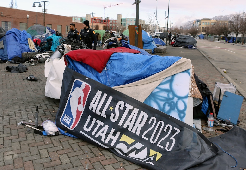 (Robin Pendergrast) A person experiencing homelessness uses a discarded All-Star Game banner as part of their shelter as Salt Lake City police patrol the area around 500 West in Salt Lake City, Thursday, March 2, 2023.