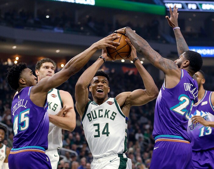 Milwaukee Bucks' Giannis Antetokounmpo (34) is fouled as he drives between Utah Jazz's Donovan Mitchell (45) and Royce O'Neale (23) during the first half of an NBA basketball game Monday, Nov. 25, 2019, in Milwaukee. (AP Photo/Aaron Gash)