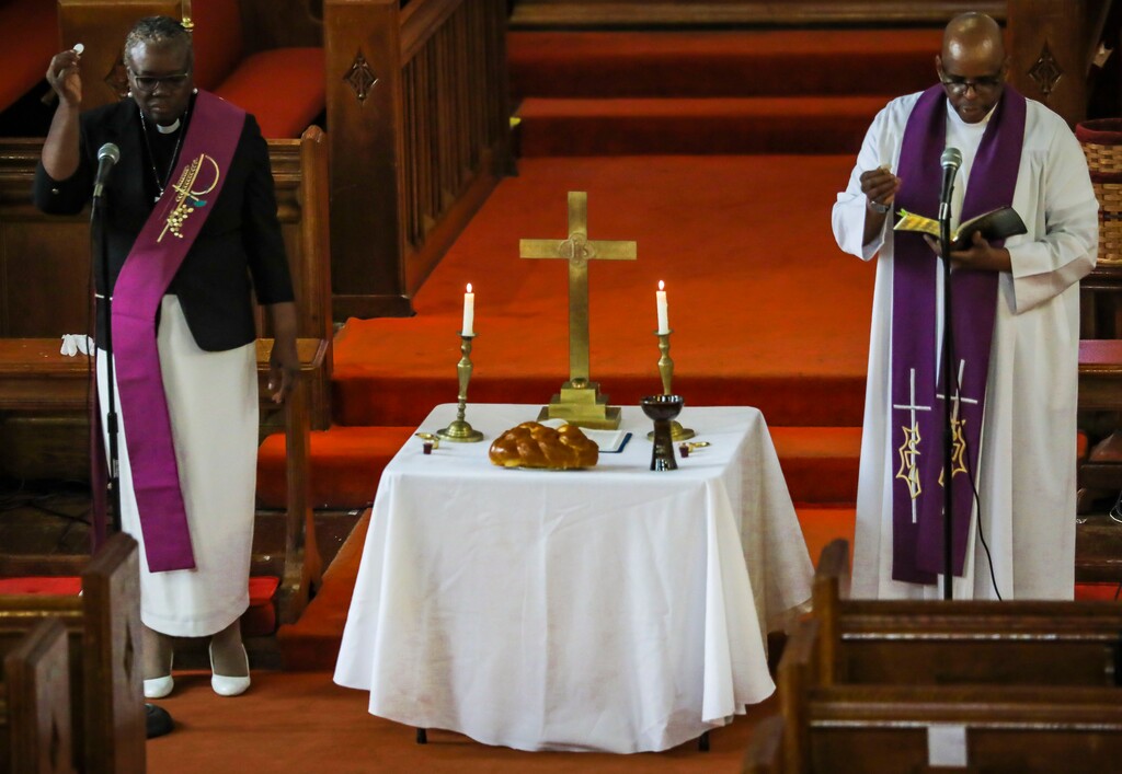 In this April 5, 2020, photo, St. Paul's Methodist Church senior pastor, the Rev. Roger Jackson, right, and youth pastor Rev. Janet Cox, offer communion during a livestream broadcast of Palm Sunday service to congregants, home-bound due to city-wide restrictions aimed at controlling the coronavirus outbreak in the Brooklyn borough of New York. Jackson and clerics of all faiths have had to also adapt the way they care for the dead. Two of his parishioners died earlier this month. (AP Photo/Bebeto Matthews)
