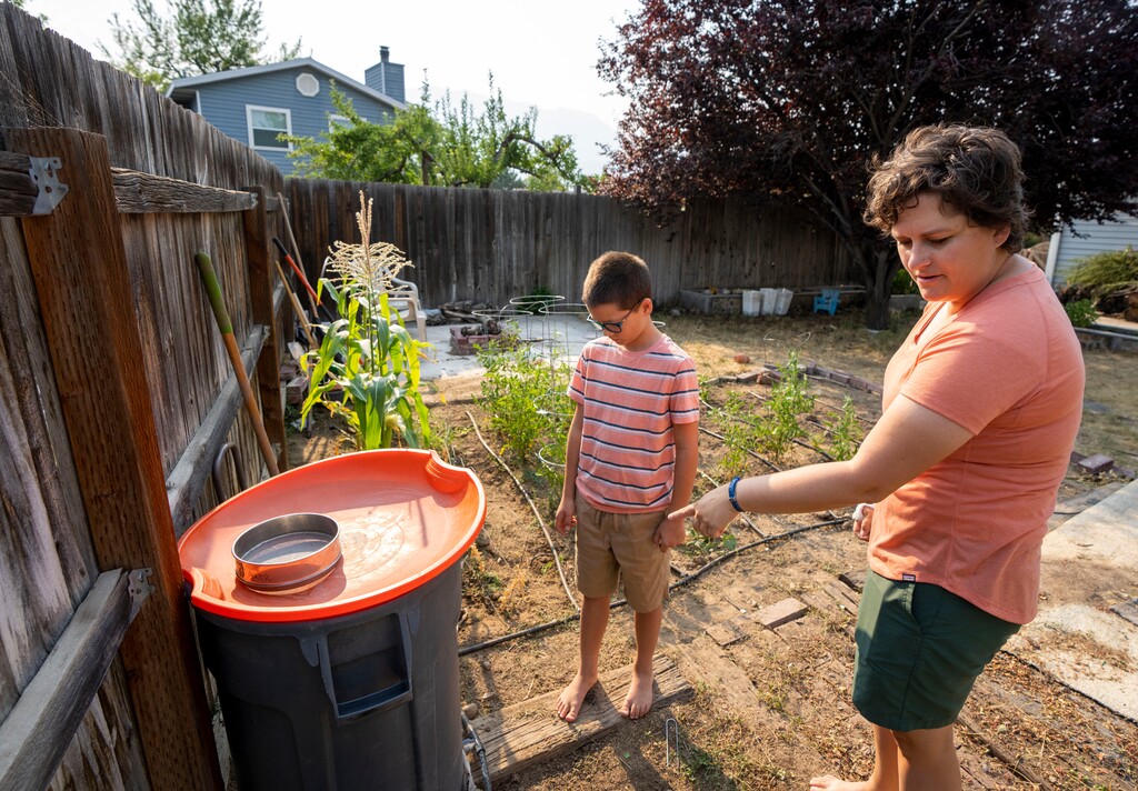 (Rick Egan | The Salt Lake Tribune) Tara Bishop and her 10-year-old son Rock, show where they store rain water to use in a drip system in their garden, at their home in Orem, on Monday, July 12, 2021.