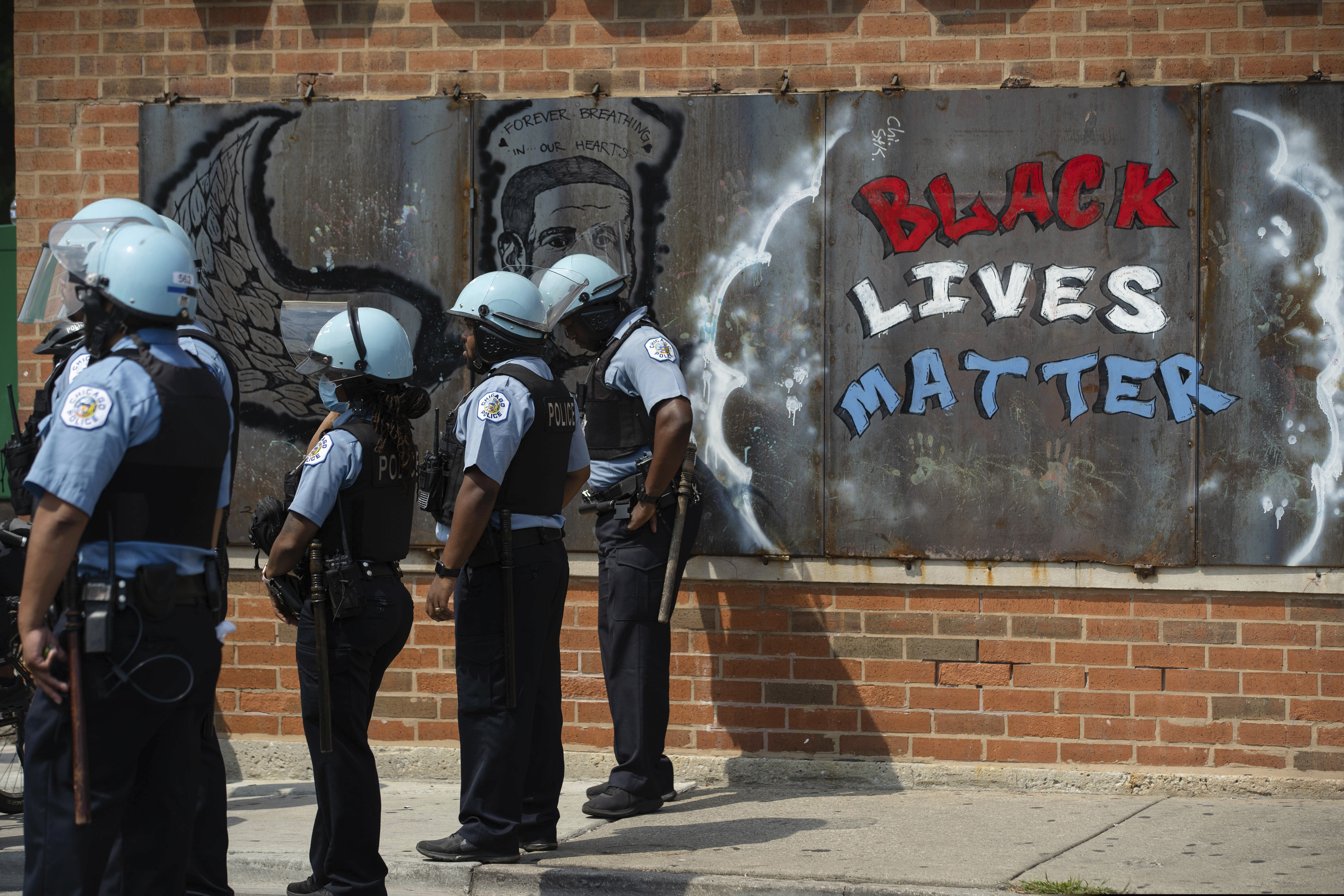 (Pat Nabong | Chicago Sun-Times via AP) In this Aug. 15, 2020, file photo, police officers stand beside a mural for George Floyd in the Chicago neighborhood of Bronzeville during an anti-police brutality protest.