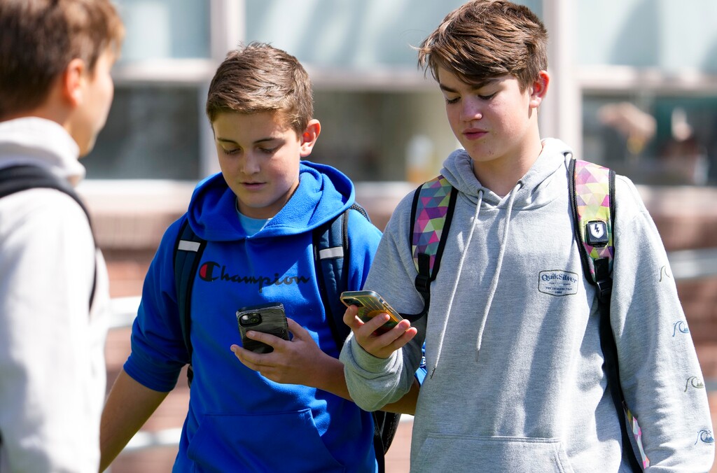(Bethany Baker | The Salt Lake Tribune) Students look at their cellphones after school as they leave Granite School District's Evergreen Junior High School on Tuesday, April 16, 2024. The district is considering implementing a universal policy banning cellphone use during school.