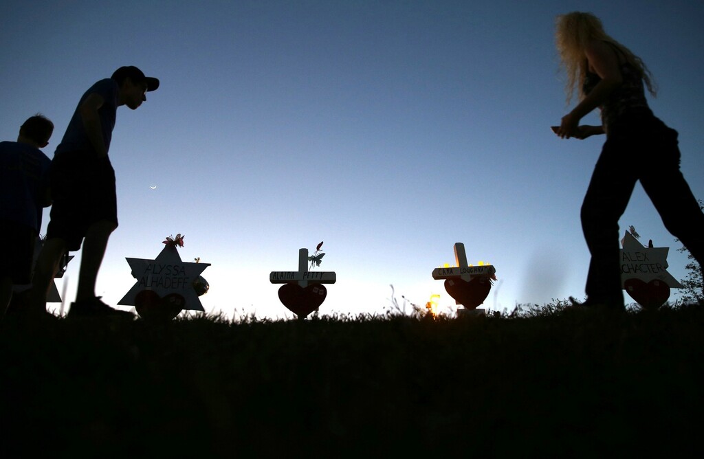 (Charles Trainor Jr | Miami Herald | The Associated Press) In this Sunday, Feb. 18, 2018, file photo, people wander among crosses on a mound in front of Marjory Stoneman Douglas High School,  where 17 crosses honor the students and teachers killed in a shooting spree on Wednesday, Feb. 14. If you want to know where mass school shootings are most likely to occur, look no farther than small-town and suburban America.