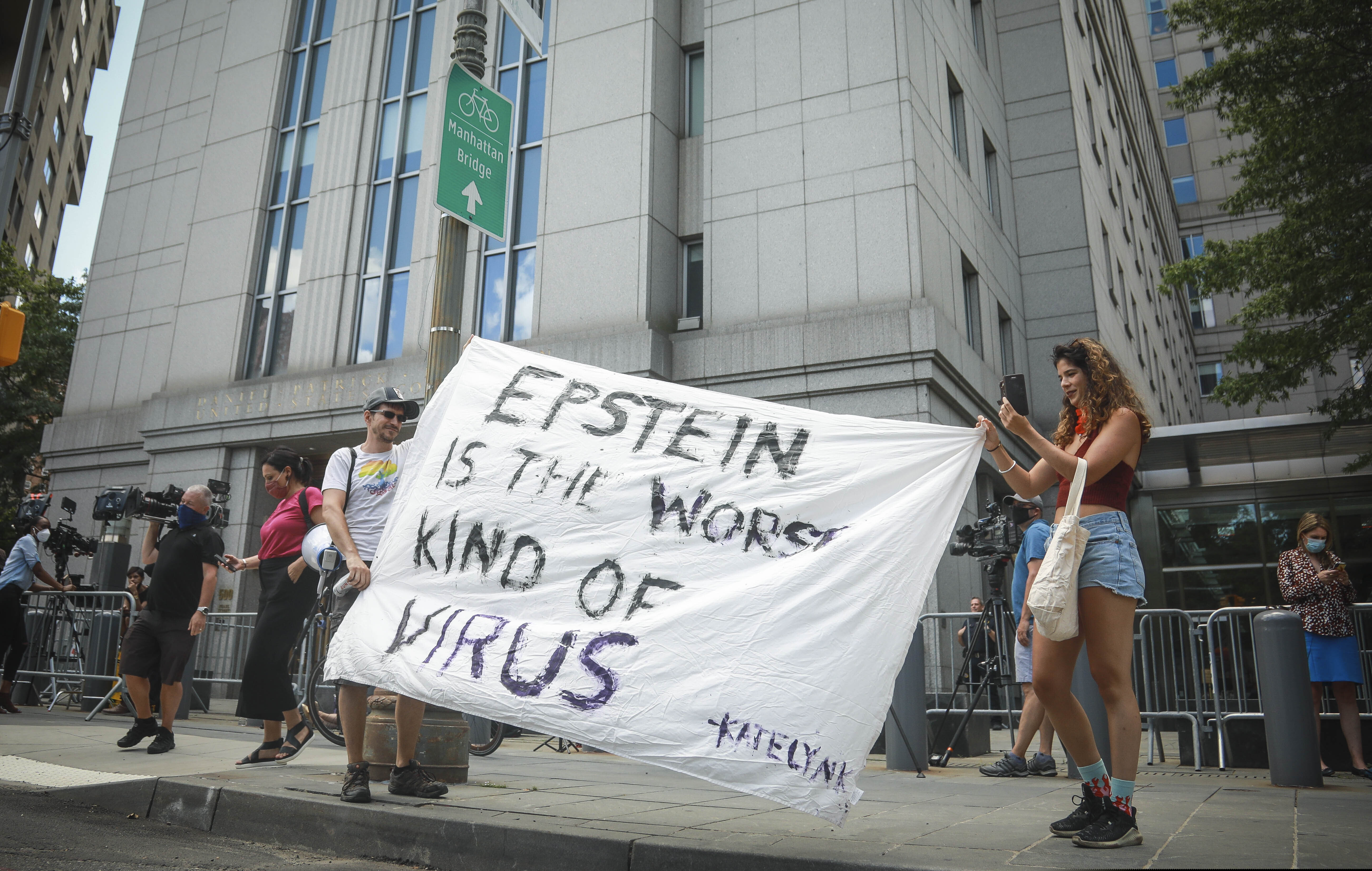 Multimedia artist Katelyn Kopenhaver, right, with help from her brother Brent Kopenhaver, unfurls a banner reading "[Jefferey] Epstein is the worst kind of virus," outside federal court where a judge held a bail hearing by video for Epstein's former girlfriend Ghislaine Maxwell, Tuesday, July 14, 2020, in New York. (AP Photo/Bebeto Matthews)