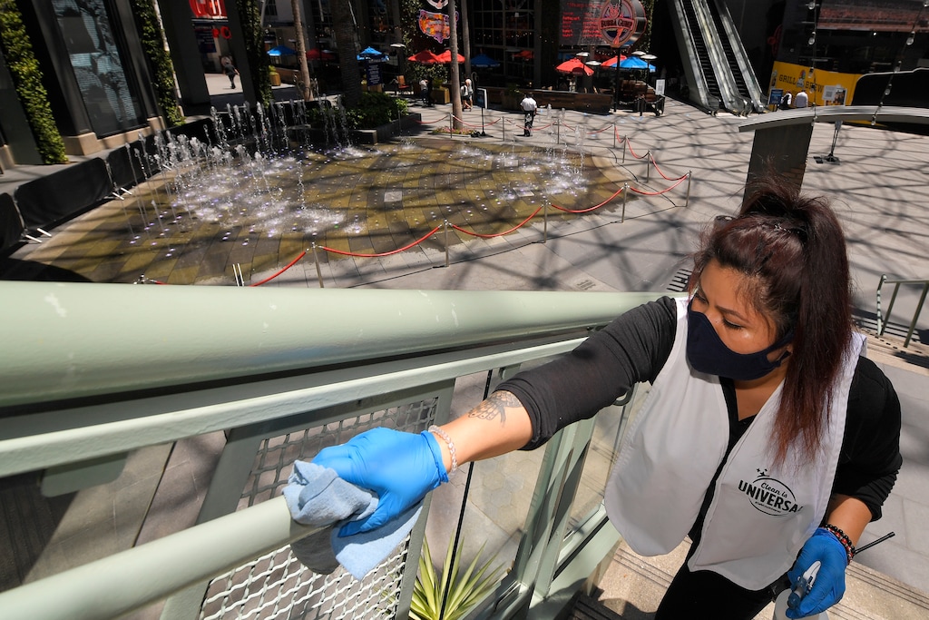 Andrea Castaneda cleans the railings at Universal CityWalk, Thursday, June 11, 2020, near Universal City, Calif. The tourist attraction, which had been closed due to the coronavirus outbreak recently re-opened. The Universal Studios tour is still closed. (AP Photo/Mark J. Terrill)