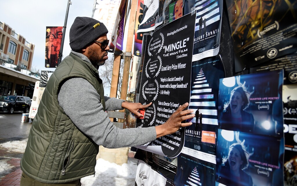 (Photo by Chris Pizzello | Invision via AP) In this Jan. 25, 2019, file photo, Ty Cooper, director of the narrative short "Mingle," puts up a poster on Main Street to promote his film during the second day of the 2019 Sundance Film Festival, in Park City, Utah. The money spent by TV and film production crews in Utah has more than doubled over the last five years as directors are drawn to the state's proximity to Los Angeles and sweeping landscapes of red bluffs, deserts and lakes, according to a state report.