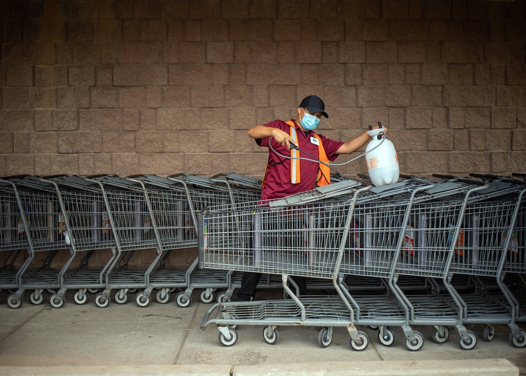 (Sharon Chischilly | The New York Times) Cordaryll Tolino disinfects shopping carts at Bashas Diné Market in Window Rock, Ariz., on Aug. 19, 2020. Native American communities have consistently had higher positivity rates for coronavirus than the general population.