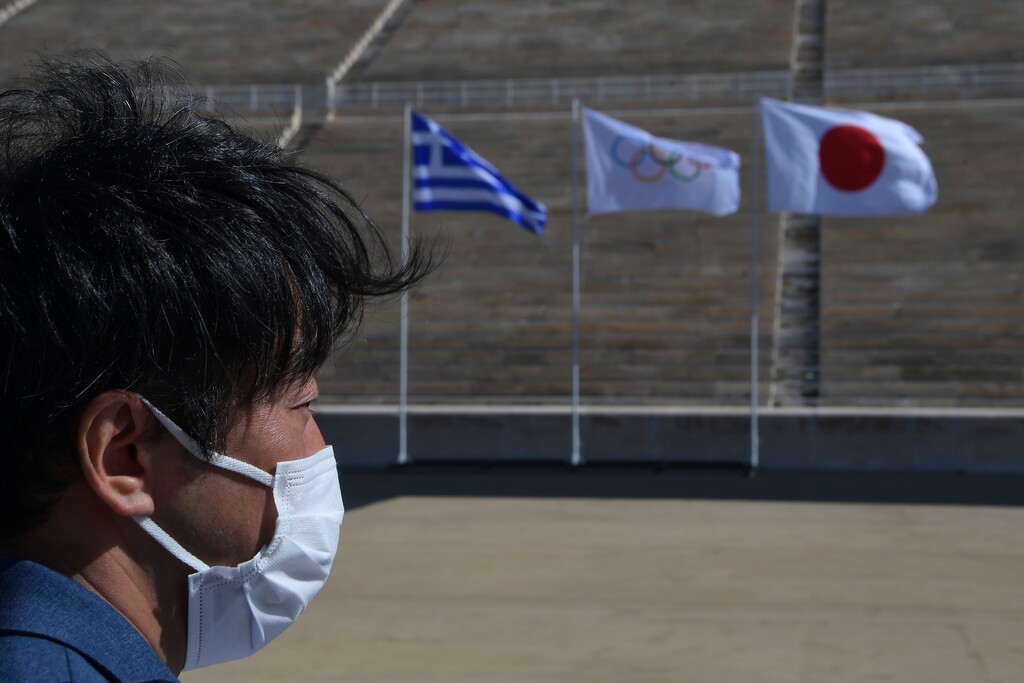 A man wearing a protective face mask attends the Olympic flame handover ceremony for the 2020 Tokyo Summer Olympics, in Athens, Thursday, March 19, 2020. The ceremony was held behind closed doors and with the presence of few members of the media because of fears over the new coronavirus. (Aris Messinis/Pool via AP)