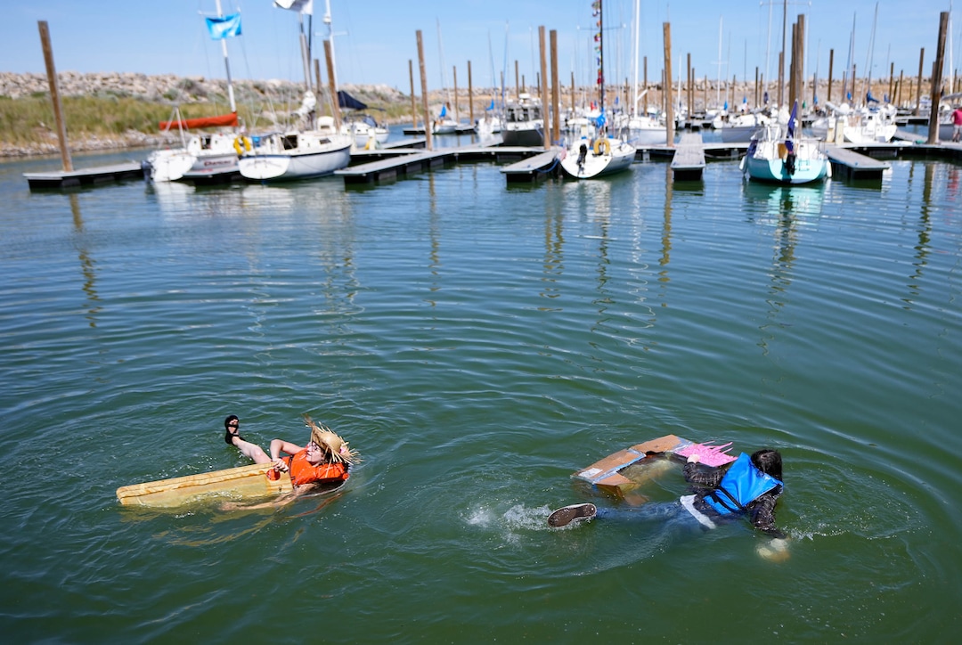 (Francisco Kjolseth  |  The Salt Lake Tribune) Amelia Brickey, left, who recently moved to the state from Chicago, takes a plunge in the Great Salt Lake to race in a large, plastic storage tub against Joe Martindale in a cardboard boat on Saturday, June 15, 2024. “Little did I know that I’d buy a sailboat in the desert,” Brickey said as she joined the festivities for the first Sailfest regatta in five years as captain of her green Ranger ’23 named Trident, in background. 
