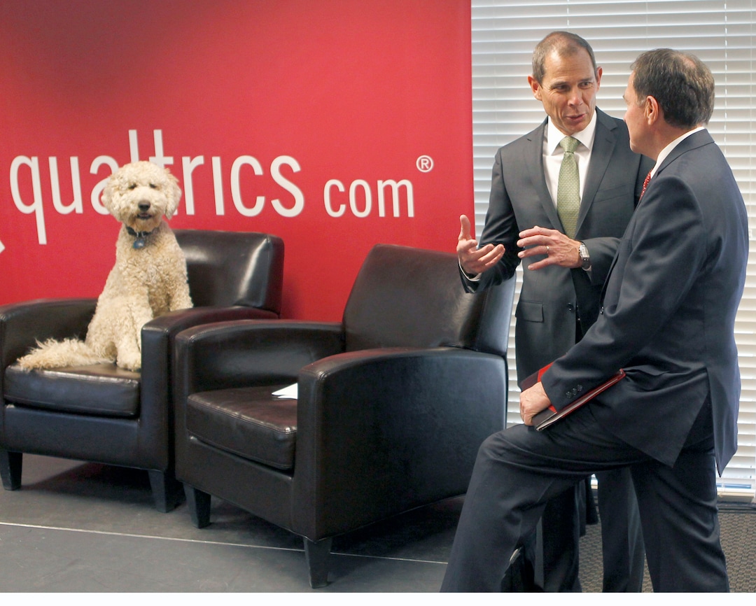 (Al Hartmann  |  Tribune file photo)  "Barnaby" takes the seat of his owner Qulatrics CEO Ryan Smith before a news announcement Tuesday May 15, 2012 in the company's headquarters in Orem as Provo Mayor John Curtis chats with Utah Governor Gary Herbert at right.    The gregarious dog pretty much has the run of the company office greeting employees and soaking up attention.