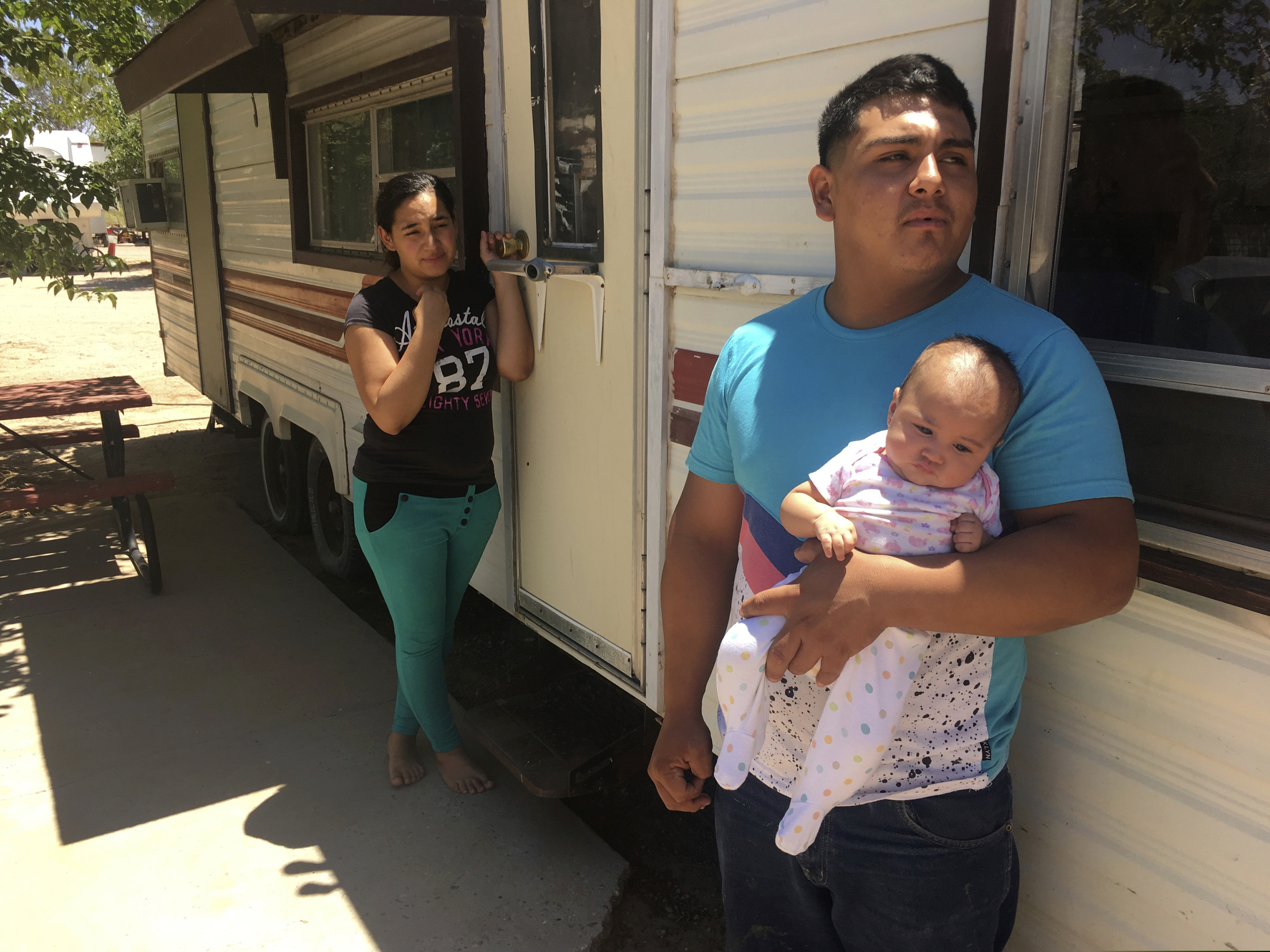 In this May 25, 2018 photo, Jose Espinoza, 18, stands out his trailer with his 4-month-old infant, Emmily, and wife, Maria Rodriguez, 19, in Vado, N.M. while speaking about making only $50 a day picking onions. The U.S. Census Bureau is using new high tech tools like aerial imagery to help get an accurate 2020 Census and avoid undercounting communities struggling with poverty. (AP Photo/Russell Contreras)