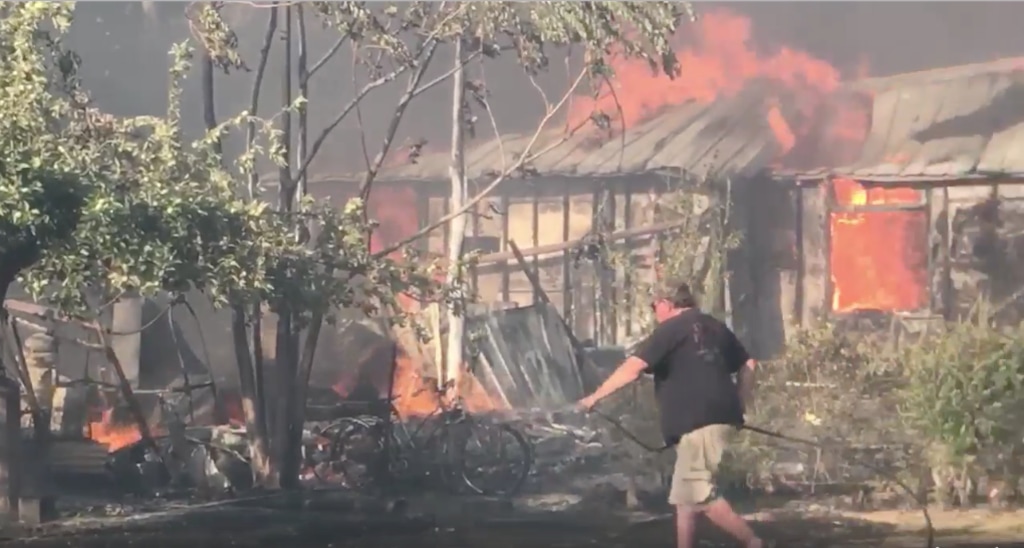 (Courtesy image from video filmed by Kevin Sheets) A Moab resident uses a garden hose to wet a lawn near a wildfire that raged through a neighborhood near Pack Creek on Tuesday night, destroying eight homes, two garages and a shop.