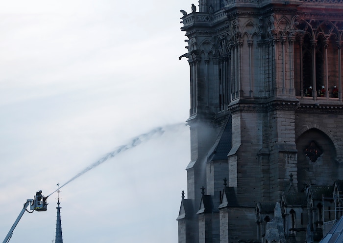 Firefighters tackle the blaze as flames and smoke rise from Notre Dame cathedral as it burns in Paris, Monday, April 15, 2019. Massive plumes of yellow brown smoke is filling the air above Notre Dame Cathedral and ash is falling on tourists and others around the island that marks the center of Paris. (AP Photo/Thibault Camus)
