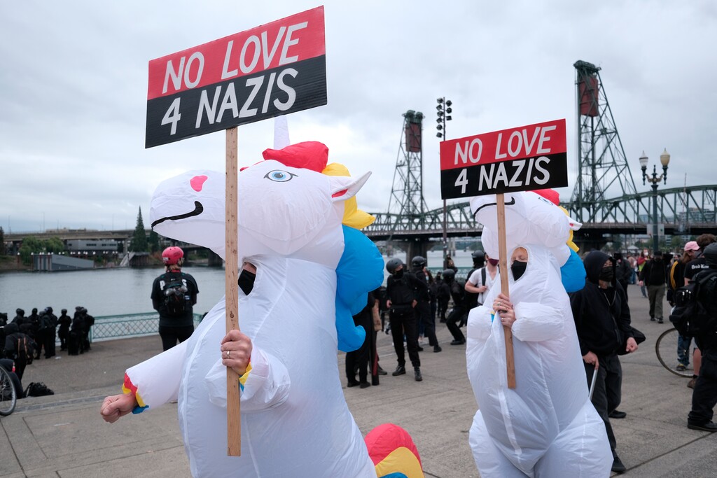 Anti-fascist protesters dressed as unicorns hold signs as people gather on the waterfront to demonstrate against a Proud Boy rally on Sunday, Aug. 22, 2021, in Portland, Ore. (AP Photo/Alex Milan Tracy)
