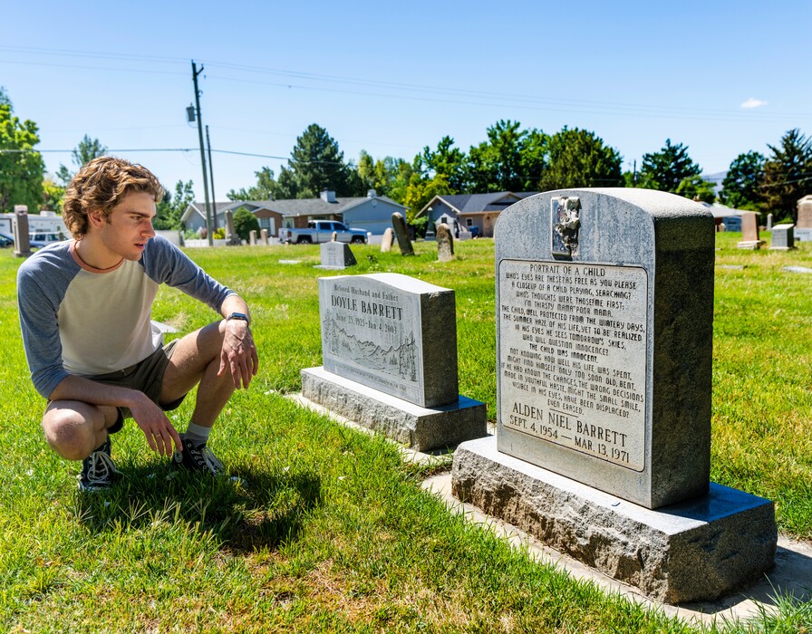 (Rick Egan | The Salt Lake Tribune)  Ian Webb, who plays Alden Barrett in a production of "Pleasant Grove Rock Opera," reads Alden's headstone at the Pleasant Grove Cemetery, on Tuesday, Aug. 16, 2022.