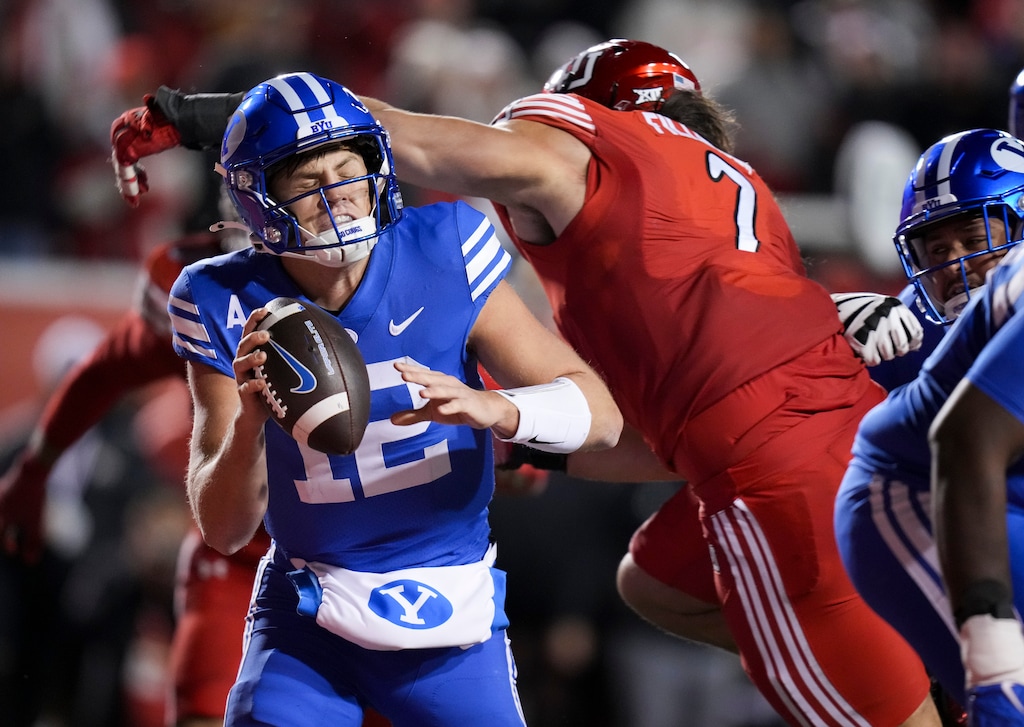 (Bethany Baker  |  The Salt Lake Tribune) Brigham Young Cougars quarterback Jake Retzlaff (12) avoids a tackle from Utah Utes defensive end Van Fillinger (7) during the game between the Utah Utes and the Brigham Young Cougars at Rice-Eccles Stadium in Salt Lake City on Sunday, Nov. 10, 2024.