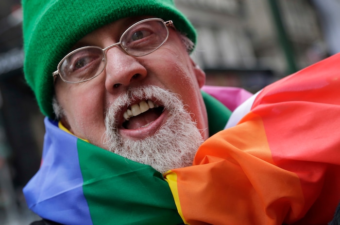 FILE - In this Monday, March 17, 2014 file photo, artist Gilbert Baker, designer of the Rainbow Flag, is draped with the flag while protesting at the St. Patrick's Day parade in New York. Baker, creator of the flag that has become a widely recognized symbol of gay rights, has died at age 65. His death was reported Friday, March 31, 2017 to the New York City medical examiner’s office. (AP Photo/Mark Lennihan)