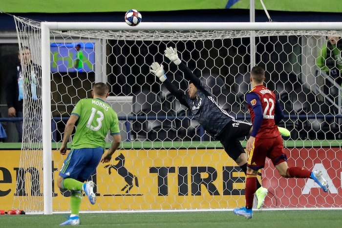 Real Salt Lake goalkeeper Nick Rimando, center, leaps as a shot goes wide and Seattle Sounders forward Jordan Morris, left, and Real Salt Lake defender Aaron Herrera, right, watch during the first half of an MLS Western Conference semifinal playoff soccer match Wednesday, Oct. 23, 2019, in Seattle. (AP Photo/Ted S. Warren)