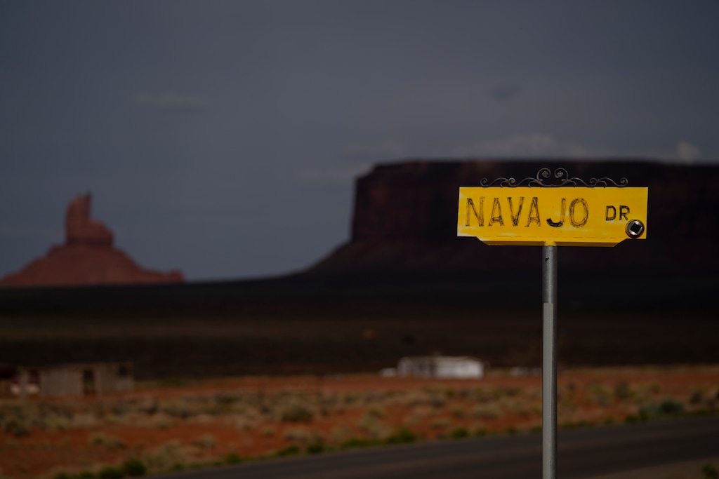 FILE - In this April 30, 2020, file photo, a sign for Navajo Drive is seen against a cloud-darkened Sentinel Mesa in Oljato-Monument Valley, Utah on the Navajo Reservation. Medical professionals serving the Navajo Nation made an urgent plea to residents Thursday, Dec. 3, 2020, to stay home as coronavirus cases rise. (AP Photo/Carolyn Kaster, File)