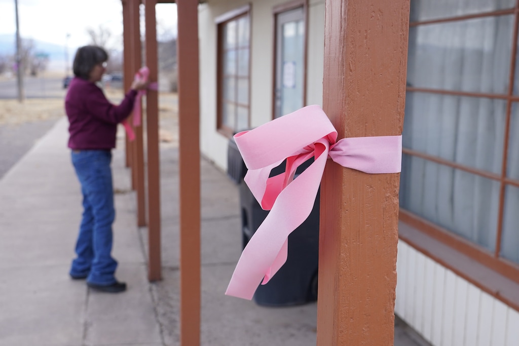 (George Frey | AP) A woman hangs a pink ribbon on a pole Thursday, March 5, 2026, in Lyman, in honor of a woman that was killed a day earlier.