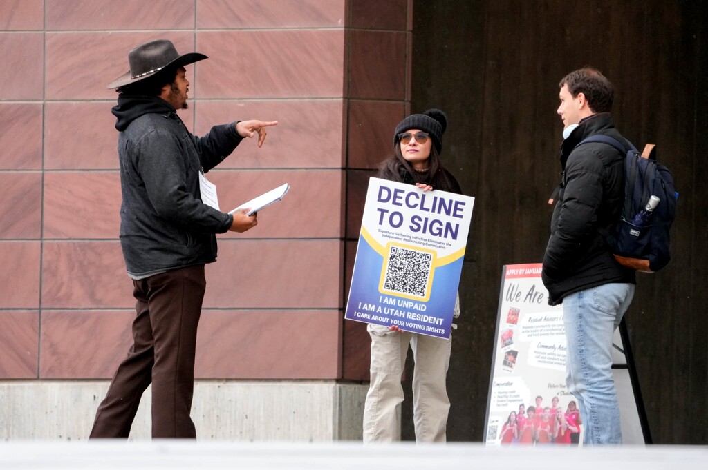 (Francisco Kjolseth | The Salt Lake Tribune) A paid signature gatherer, left, reaches out to Utah voters at the University of Utah Marriott Library in the ongoing effort to repeal Proposition 4, the 2018 voter-approved ballot initiative on redistricting, on Thursday, Jan. 8, 2026. An unpaid volunteer, center, was on hand to oppose the effort being put forth by the Utah Republican Party.