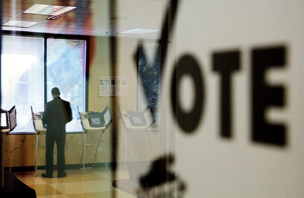 A voter is reflected in the glass frame of a poster while casting a ballot during early voting in Atlanta, Tuesday, Nov. 1, 2016.  (AP Photo/David Goldman)