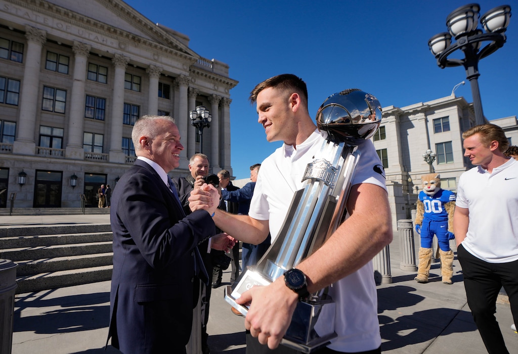 (Francisco Kjolseth  | The Salt Lake Tribune) BYU President Shane Reese, greets BYU quarterback Jake Retzlaff as he holds the 2024 Alamo Bowl championship trophy during a visit to the Utah Capitol to be recognized by the Utah legislature for the team’s achievements on Wednesday February. 26, 2025.
