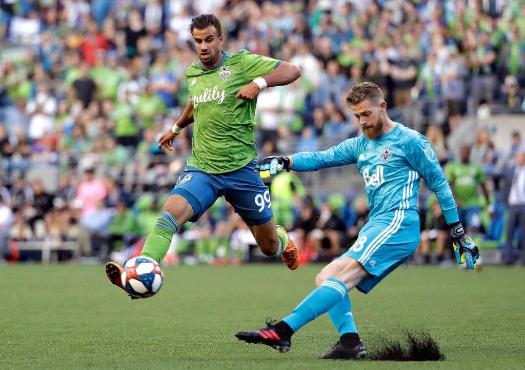 Vancouver Whitecaps goalie Zac MacMath, right, kicks the ball just past Seattle Sounders' Justin Dhillon in the first half of an MLS soccer match Saturday, June 29, 2019, in Seattle. (AP Photo/Elaine Thompson)