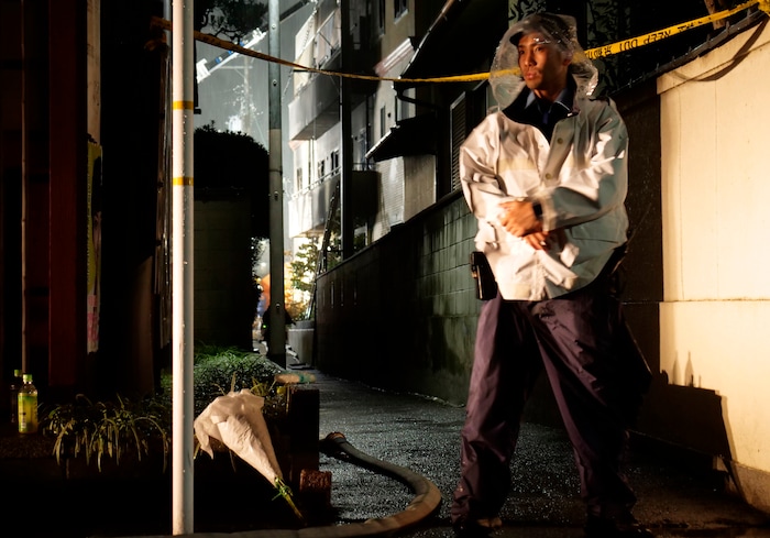 (Hiromi Tanoue | AP Photo) A police officers stands by flowers laid near Kyoto Animation building following a fire in Kyoto, western Japan, Thursday, July 18, 2019. The fire broke out in the three-story building in Japan's ancient capital of Kyoto, after a suspect sprayed an unidentified liquid to accelerate the blaze, Kyoto prefectural police and fire department officials said.