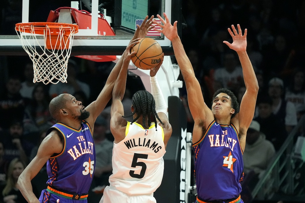 Utah Jazz forward Cody Williams (5) slips between Phoenix Suns forward Kevin Durant (35) and center Oso Ighodaro (4) to score during the second half of an NBA basketball game Saturday, Jan. 11, 2025, in Phoenix. (AP Photo/Ross D. Franklin)