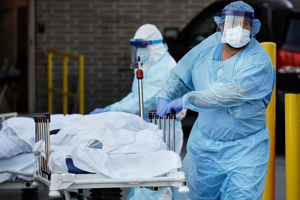 (John Minchillo  |  AP)  Medical workers wearing personal protective equipment wheel bodies to a refrigerated trailer serving as a makeshift morgue at Wyckoff Heights Medical Center, Monday, April 6, 2020, in the Brooklyn borough of New York. The new coronavirus causes mild or moderate symptoms for most people, but for some, especially older adults and people with existing health problems, it can cause more severe illness or death.