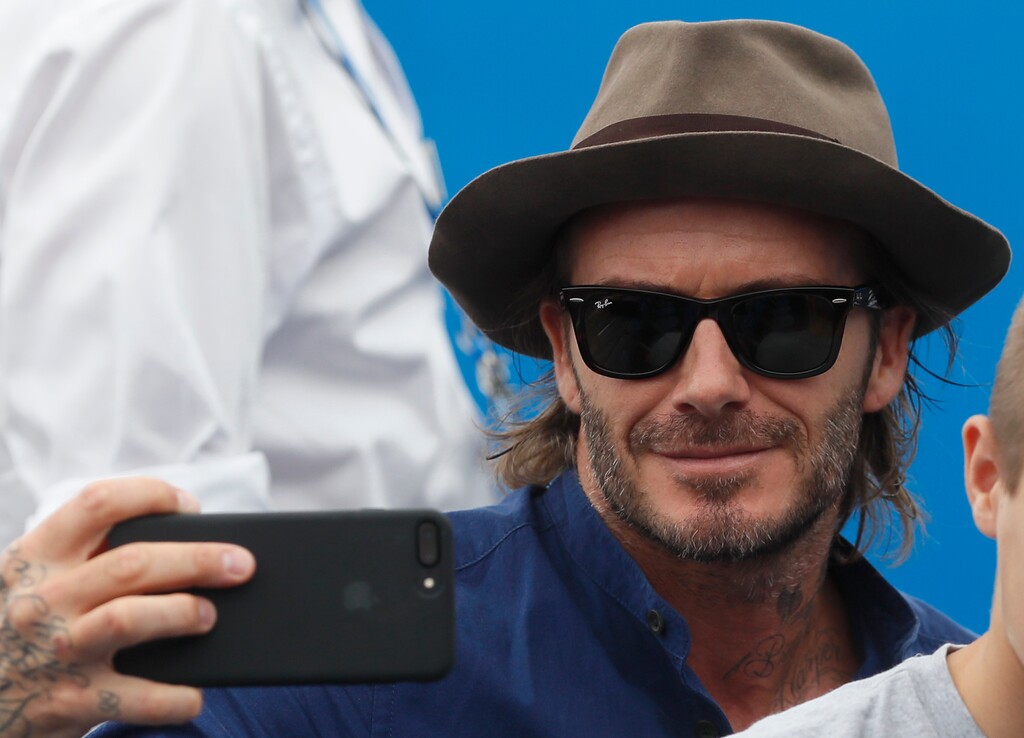 Former England soccer player David Beckham takes a selfie with his son as they watch the match between Sam Querrey of the United States and Jordan Thompson of Australia during day four of the Queen's Club tennis tournament in London, Thursday, June 22, 2017. (AP Photo/Kirsty Wigglesworth)