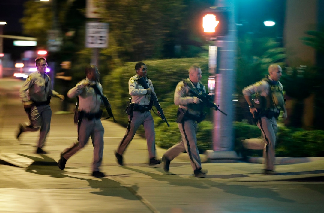 Police run to cover at the scene of a shooting near the Mandalay Bay resort and casino on the Las Vegas Strip, Sunday, Oct. 1, 2017, in Las Vegas. Multiple victims were being transported to hospitals after a shooting late Sunday at a music festival on the Las Vegas Strip. (AP Photo/John Locher)