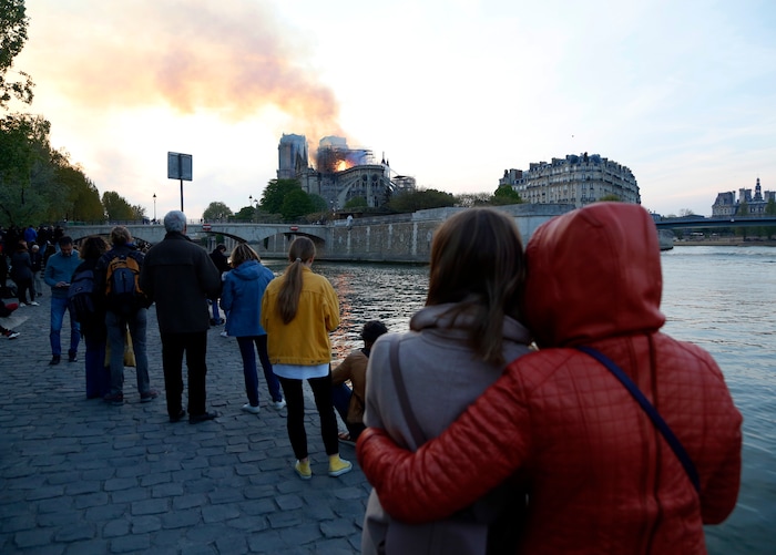 People watch as flames and smoke rise from Notre Dame cathedral as it burns in Paris, Monday, April 15, 2019. Massive plumes of yellow brown smoke is filling the air above Notre Dame Cathedral and ash is falling on tourists and others around the island that marks the center of Paris. (AP Photo/Thibault Camus)