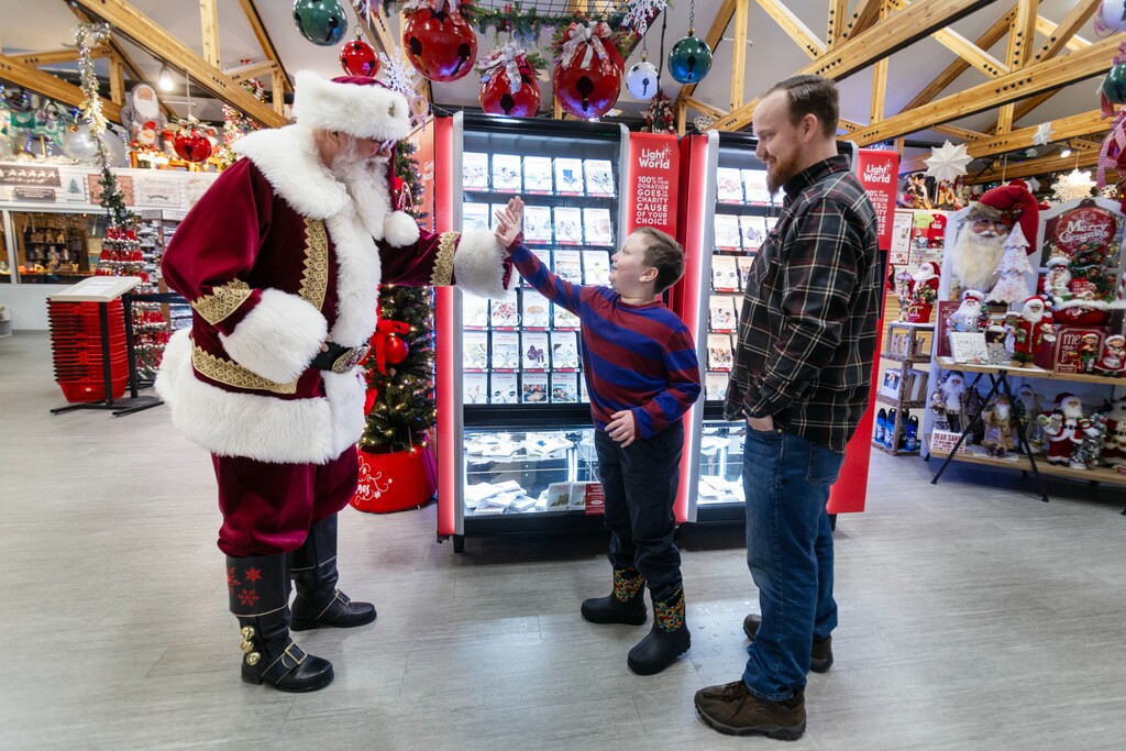 (The Church of Jesus Christ of Latter-day Saints) Santa Claus gives Patrick Moulton a high-five in front of Light the World Giving Machines at Santa Claus House in North Pole, Alaska, on Friday, Nov. 22, 2024. Santa told Patrick he was not on the nice list, he was on the "extra nice list."