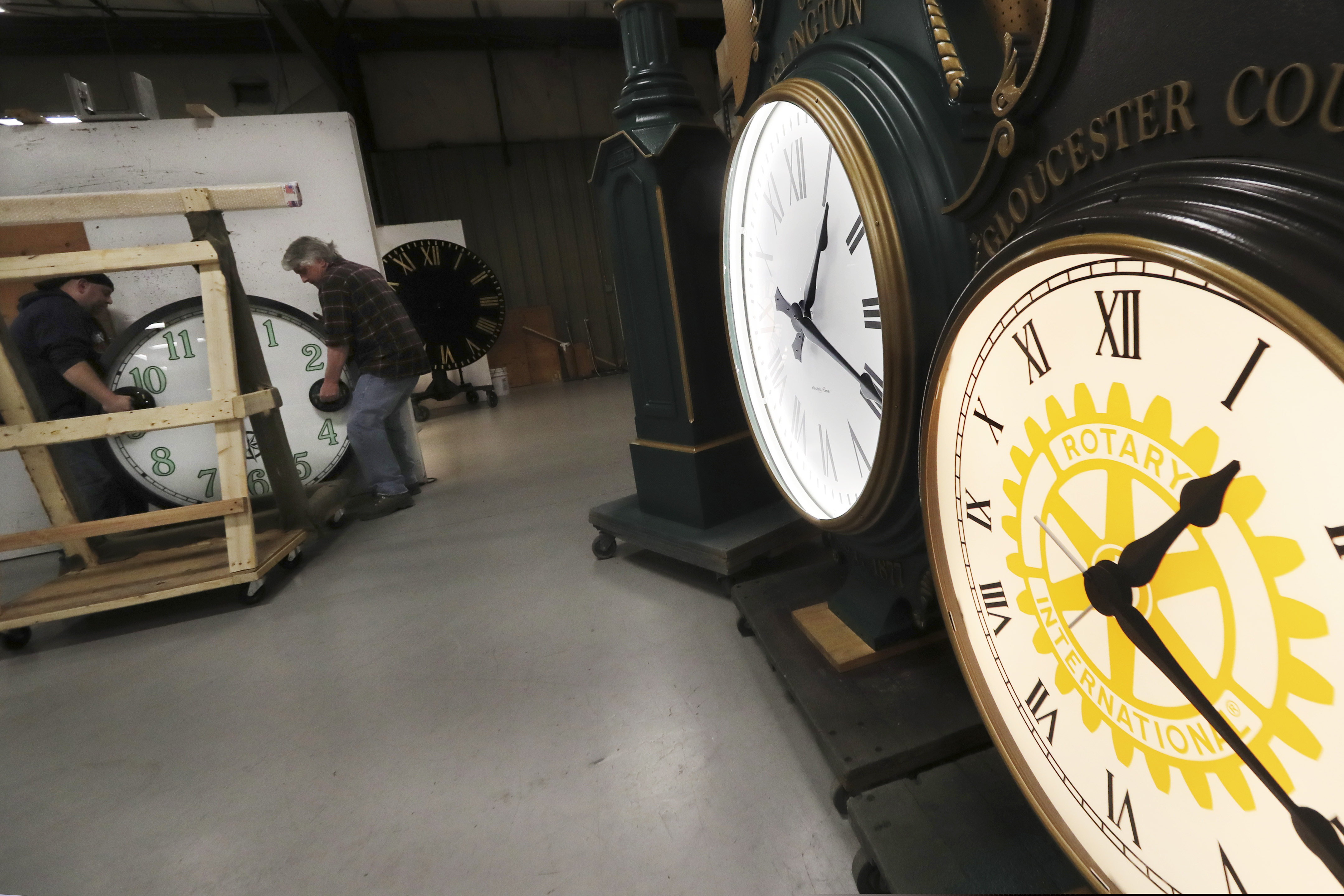 (Charles Krupa | The Associated Press) In this Thursday, March 5, 2020 photo, workers carry a clock, created for a New York City client, onto the testing wall at the Electric Time Company, in Medfield, Massachusetts. 